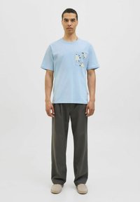 Lyseblå bomulds T-shirt med en blomster-mønstret lomme, parret med løse grå bukser og beige slip-on sko. Enkel design, afslappet pasform.