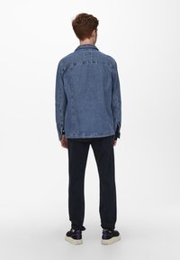 Jeansjacke in Mittelblau, mit lockerer Passform, Knopfverschluss und langen Ärmeln. Getragen mit dunklen Hosen und Sneakers. Einfaches Kragen Design.