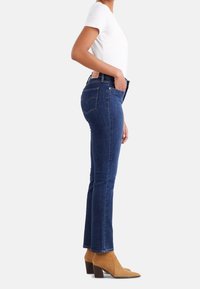 Jeans de mezclilla azul con una silueta ajustada, cintura alta, diseño de cinco bolsillos y costuras en contraste. Combinados con botas de tobillo color canela.