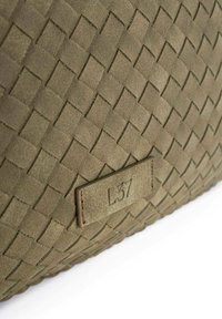 Sac en daim vert avec une texture tissée et des motifs rectangulaires. Une étiquette en cuir portant l'inscription "L37" est positionnée sur un côté.