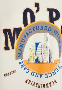 Texto y diseño abstracto de paisaje urbano con "FABRICADO CON CONSCIENCIA Y CUIDADO" y grandes letras "M O P" sobre fondo de tela clara.