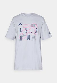T-shirt en coton blanc avec un graphisme géométrique en rose et bleu marine, accompagné de texte et de chiffres. Manches courtes et encolure ras du cou.
