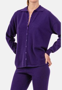 Lila Strick-Cardigan mit Kragen, Knopfleiste und langen Ärmeln. Der Stoff hat eine weiche Textur und eine lockere Passform.