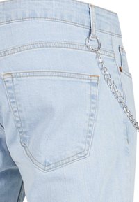 Los jeans de denim azul claro presentan una cadena de plata unida a un lazo del cinturón, con dos bolsillos traseros y sutiles detalles de costura.
