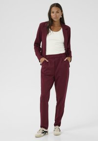 Ensemble en bourgogne comprenant un blazer ajusté et un pantalon sur mesure. Le blazer possède un col à revers, et le pantalon est doté de poches latérales pour plus de commodité.