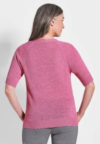Rosa Kurzarmpullover mit strukturierter Oberfläche, Raglanärmeln und gerippten Bündchen. Getragen mit gemusterten schwarz-weißen Karohosen.