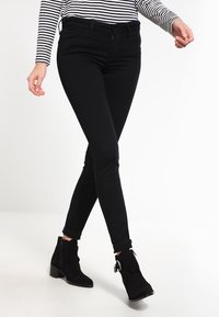 Jeans negros ajustados hechos de material elástico, con un corte slim, cintura de media altura y puños enrollados, combinados con botas negras hasta el tobillo.