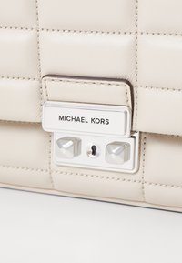 Borsa in pelle crema con design trapuntato, accessori in argento e una funzione di chiusura. La placca del logo riporta "MICHAEL KORS" in evidenza.