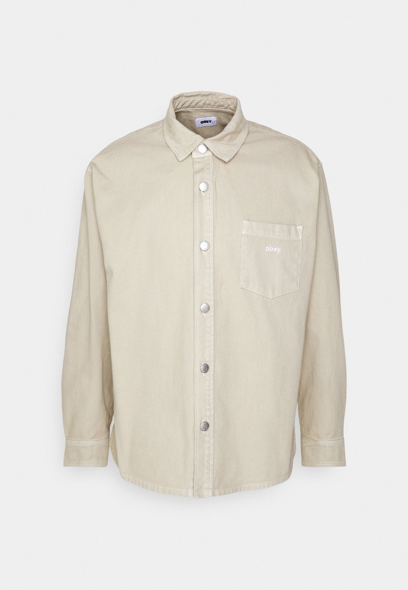 Beige long-sleeve button-up shirt with collar, chest pocket displaying "obey" text, and silver snap buttons down the front.