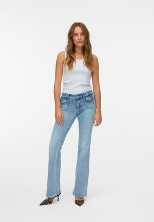 Light blue flared jeans with a mid-rise waist, five pockets, and subtle whiskering. Paired with a light gray tank top and black polka dot heels.