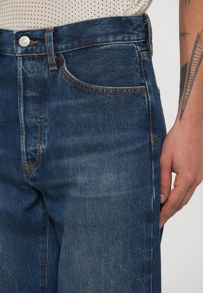 Σκούρο μπλε τζιν με ψηλή μέση, με πορτοκαλί ραφές και κλασικό σχέδιο με πέντε τσέπες. Μαλακή υφή και μοντέρνο κόψιμο.