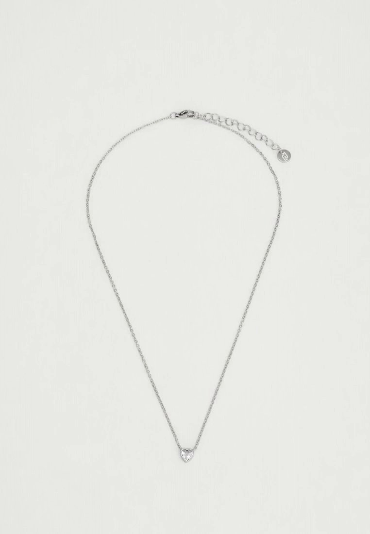 Un fin collier à chaîne de ton argenté, avec un petit pendentif en forme de cœur et un fermoir réglable, présenté sur un fond clair.