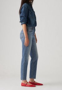 Camisa de mezclilla azul oscuro, vaqueros deslavados de corte recto y bailarinas rojas con detalle de correa, vistas de lado.