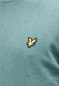 Pulover tricotat bleu deschis, cu țesătură texturată și logo mic brodat cu un păsărel galben pe partea stângă a pieptului.