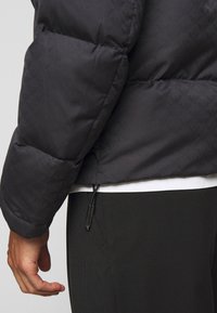 Musterniga mustriga musta pehme jope, millel on elastsed randmepaelad ja nööriga hem, koos musta alusseelikuga.