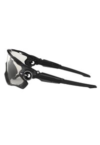 Occhiali da sole sportivi neri con design avvolgente, lenti trasparenti e montatura nera strutturata. Templi regolabili per una vestibilità sicura.