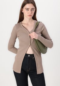 Cardigan marrone a coste, con bottoni e scollo a V, indossato con jeans blu scuro a vita alta e una borsa a spalla verde.