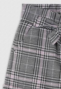 Gonna houndstooth bianco e nero con dettagli fucsia, caratterizzata da una vita alta e un dettaglio di cintura annodata. Realizzata in tessuto tessuto testurizzato.