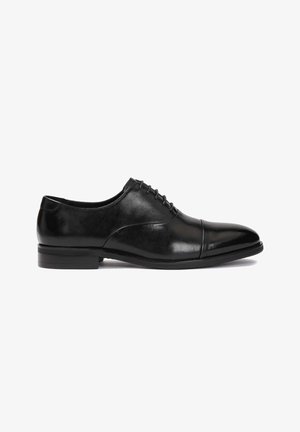 Chaussure de ville en cuir noir comprenant une finition lisse, un bout arrondi, des détails de couture subtils et un petit talon empilé. Design classique à lacets.