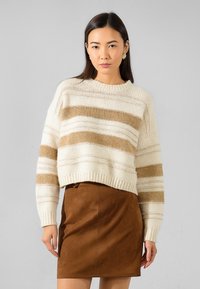 Maglione lavorato a maglia crema con strisce orizzontali marroni, dotato di orlo a coste e scollatura rotonda; abbinato a una mini gonna in suede marrone.