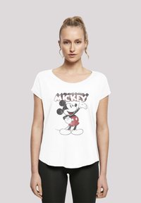 Bílý tričko s krátkým rukávem, které zobrazuje grafiku Mickey Mouse v červených šortkách. Tričko má volný střih a kulatý výstřih.
