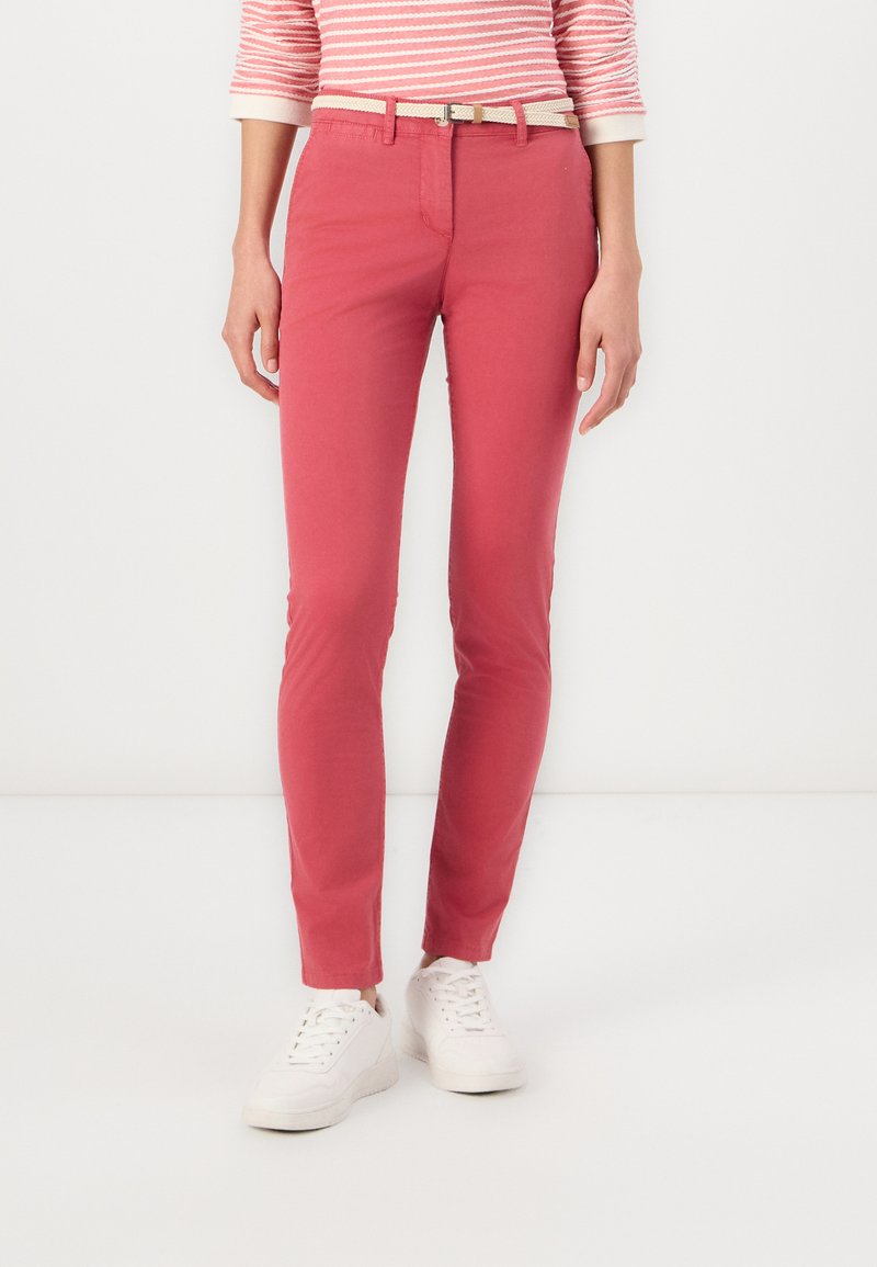 Pantalones de mezcla de algodón rojos con corte slim, que cuentan con un pequeño cinturón, combinados con zapatillas blancas y una camiseta de manga larga a rayas.
