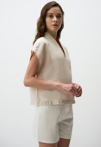 Beige linnen top met korte mouwen en een V-hals, gecombineerd met crèmekleurige shorts. Eenvoudige, losse pasvorm zonder zichtbare patronen of accenten.