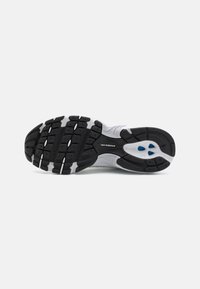 Semelle de chaussure de sport en noir et blanc avec grip en caoutchouc texturé, arborant un logo bien visible et des motifs de traction distincts.
