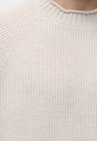 Pull tricoté couleur crème avec encolure ronde côtelée et motif tricot texturé sur les épaules et la poitrine.