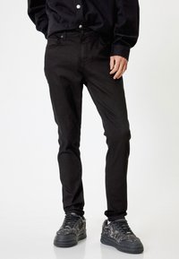 Musta farkkukangas, joka on slim fit -mallinen, varustettuna nappisuljennalla, sivutaskuilla ja hienovaraisilla ommel yksityiskohdilla. Yhdistetty teksturoiduilla mustilla tennareilla.