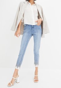 Světle modré džíny s cropped střihem, s bílou krajkovou výšivkou na lemu. Spárováno s bílou košilí na knoflíky a béžovým blejzrem.