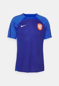 Camiseta deportiva azul de manga corta, con un diseño texturizado en los hombros, logo de Nike y un emblema de león rojo-naranja en el pecho.