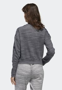 Sudadera recortada de color gris oscuro con tejido texturizado, mangas largas y acentos estampados a lo largo de los hombros. Combinada con pantalones gris claro.