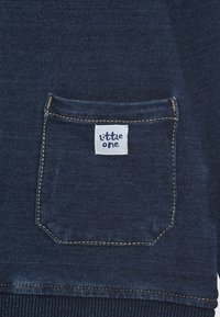 Denim sweatshirt with a front pocket, featuring a stitched label "little one." Fabric has a textured, dark blue pattern with contrasting gold stitching.