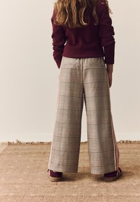 Pantalons larges à carreaux beige avec accents roses, dotés d'une taille haute et de bandes latérales. Associés à des chaussures bordeaux.