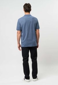 Modrá polokošeľa s krátkym rukávom a golierom, kombinovaná s čiernymi úzkymi džínsami a bielymi teniskami. Jednoduchý dizajn, bavlnený materiál.