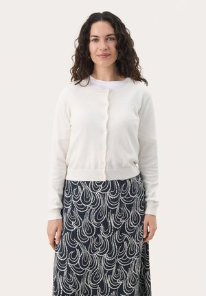 White cardigan with a crew neckline, button closure, and ribbed hem, paired with a navy skirt featuring a white swirling pattern.