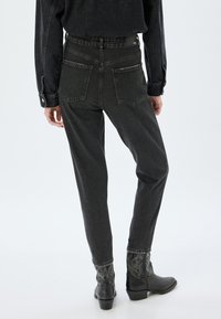Jeans de denim negro con una cintura alta, piernas estrechas y dos bolsillos traseros. Combinados con botas de vaquero negras bordadas.