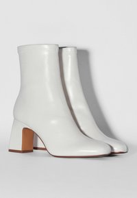 Botines de cuero blanco hasta el tobillo con una textura suave,punteras cuadradas y un tacón cuadrado. Detalles de costura a lo largo de los bordes. Diseño clásico.