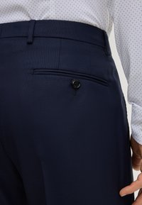 Pantaloni eleganti blu navy in tessuto strutturato, con tasca posteriore chiusa da bottone e vestibilità sartoriale.