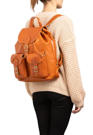 Sac à dos en cuir tan avec un rabat arrondi, des boucles décoratives, deux poches avant et des bretelles réglables. Fini texturé.