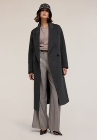 Abrigo de lana gris con diseño de doble botonadura, combinado con un suéter rosa claro y pantalones de pierna ancha a rayas, acentuado por un sombrero de cubo azul.