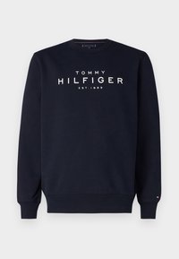 Sweatshirt bleu marine en coton avec un col rond. Présente le logo blanc "TOMMY HILFIGER" et le détail "EST. 1985". Texture douce.