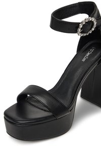 Sandale din piele neagră cu platformă, cu vârf deschis rotund, bretele late și o cataramă decorativă cu rhinestone pe curea.