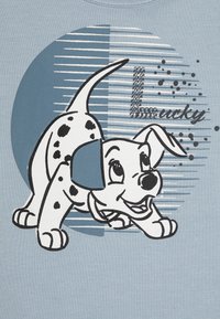 Gråblå T-shirt med en tecknad dalmatiner-valp, svarta fläckar, omgiven av svart kontur, mot en cirkulär grafik med streck och ordet "Lucky."
