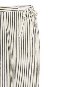 Pantalon beige et marine à rayures verticales avec taille haute et détail à nouer sur le côté sur un fond uni.