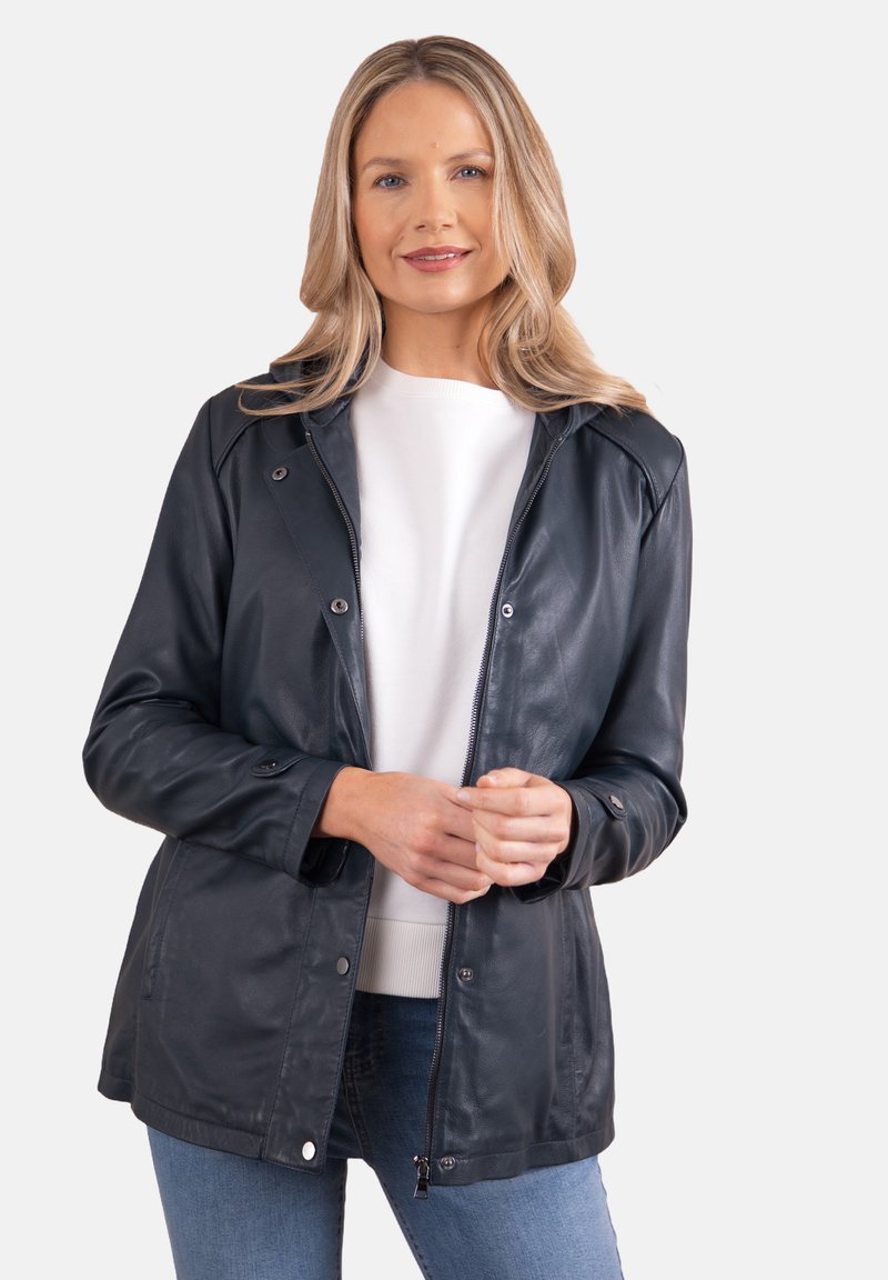 Black leather jacket with a zip front, snap buttons, and a relaxed fit. Features a hood and soft texture, paired with a white top and jeans.