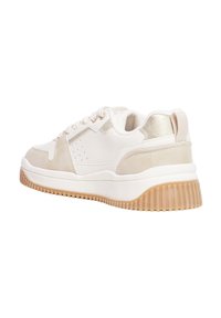 Zapatillas blancas con ante beige y acentos metálicos, que presentan una suela de goma texturizada, un diseño de encaje y detalles perforados en los laterales.