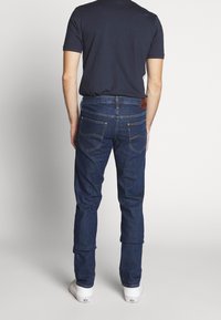 Tmavě modré džíny s přímým střihem, s dvěma zadními kapsami a hnědou koženou nášivkou. Nošeny s přiléhavým námořnicky modrým tričkem.