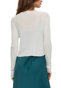 Biały, prążkowany top z długim rękawem o skróconym kroju i okrągłym dekoltem, noszony na zwiewnej tealowej spódnicy. Miękka, lekka dzianina.